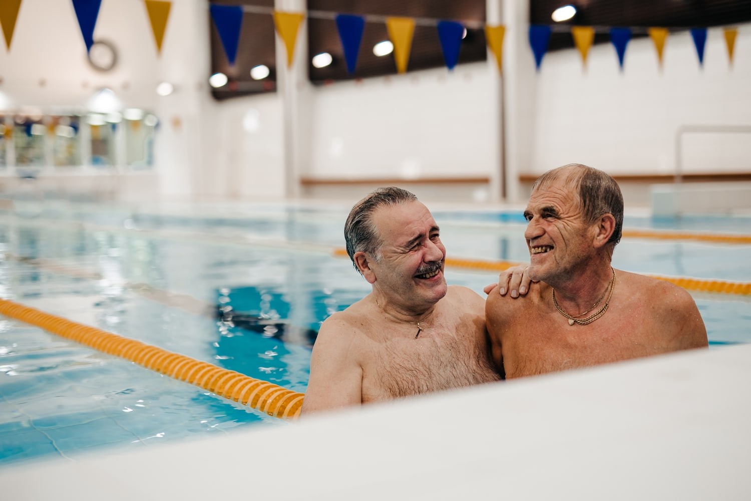 Kaksi miestä uima-altaassa uimahallissa. Molemmat hymyilevät.